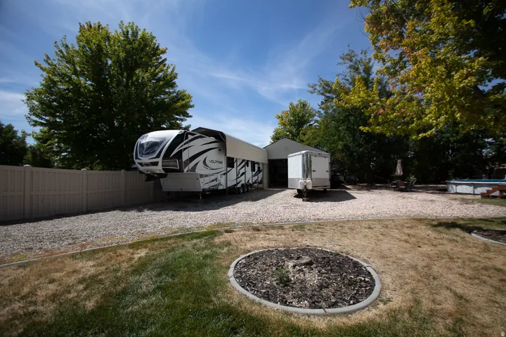 Gravel driveway and parking area, mature trees, and a privacy fence
