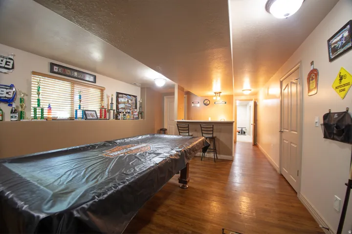 Spacious recreation room featuring wood-finish flooring, recessed and pendant lighting throughout, and multiple storage areas