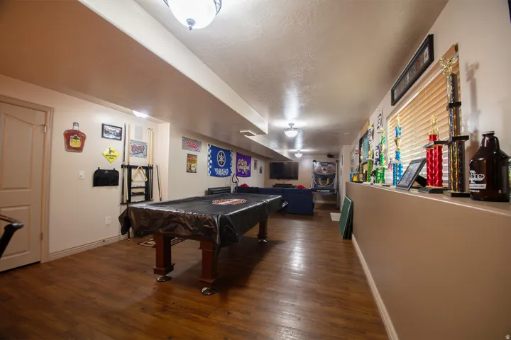 Finished basement recreation room featuring wood-finish flooring, recessed ceiling lighting, and built-in bar cabinetry with beverage storage
