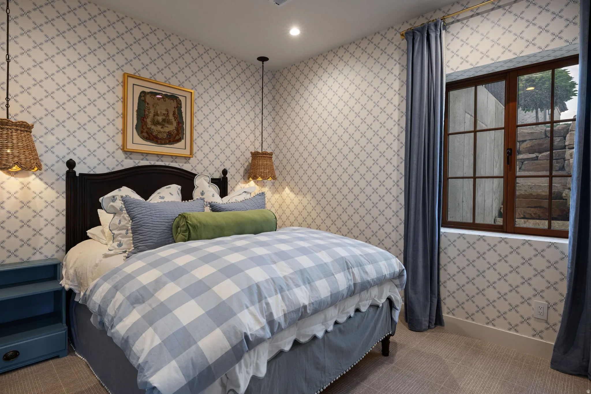 Charming bedroom featuring a black metal bed frame, patterned wallcovering throughout, pendant lighting fixtures, and wood-frame French doors with multi-pane glazing