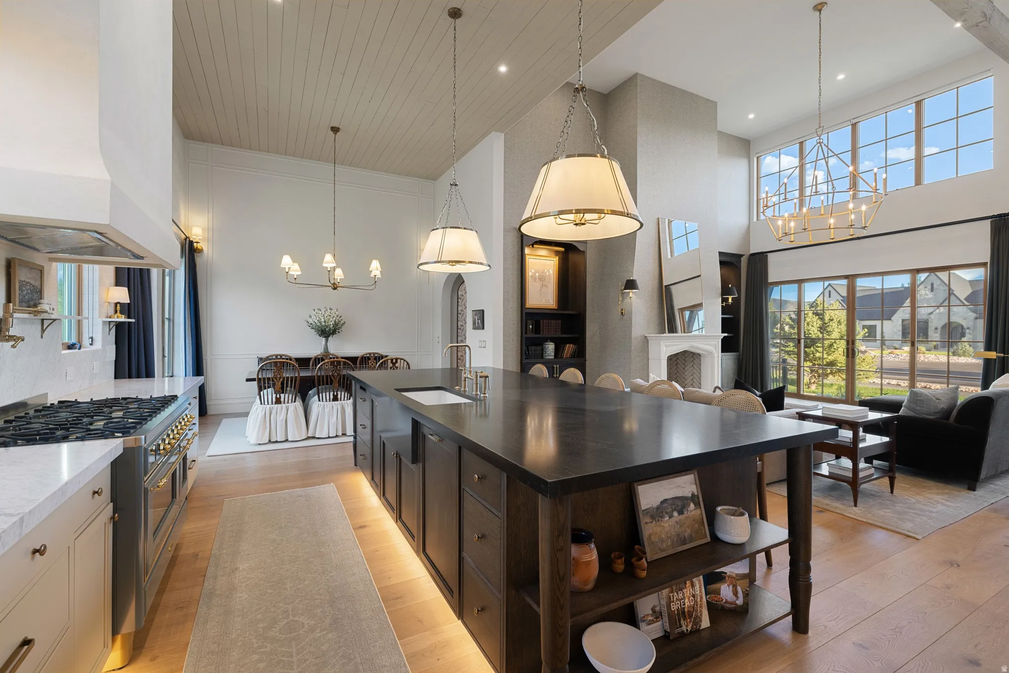 Open-concept kitchen and living area featuring a large center island with dark wood cabinetry and open shelving, pendant lighting, stainless steel appliances including a professional-style range, white cabinetry, wood-finish flooring, and expansive window