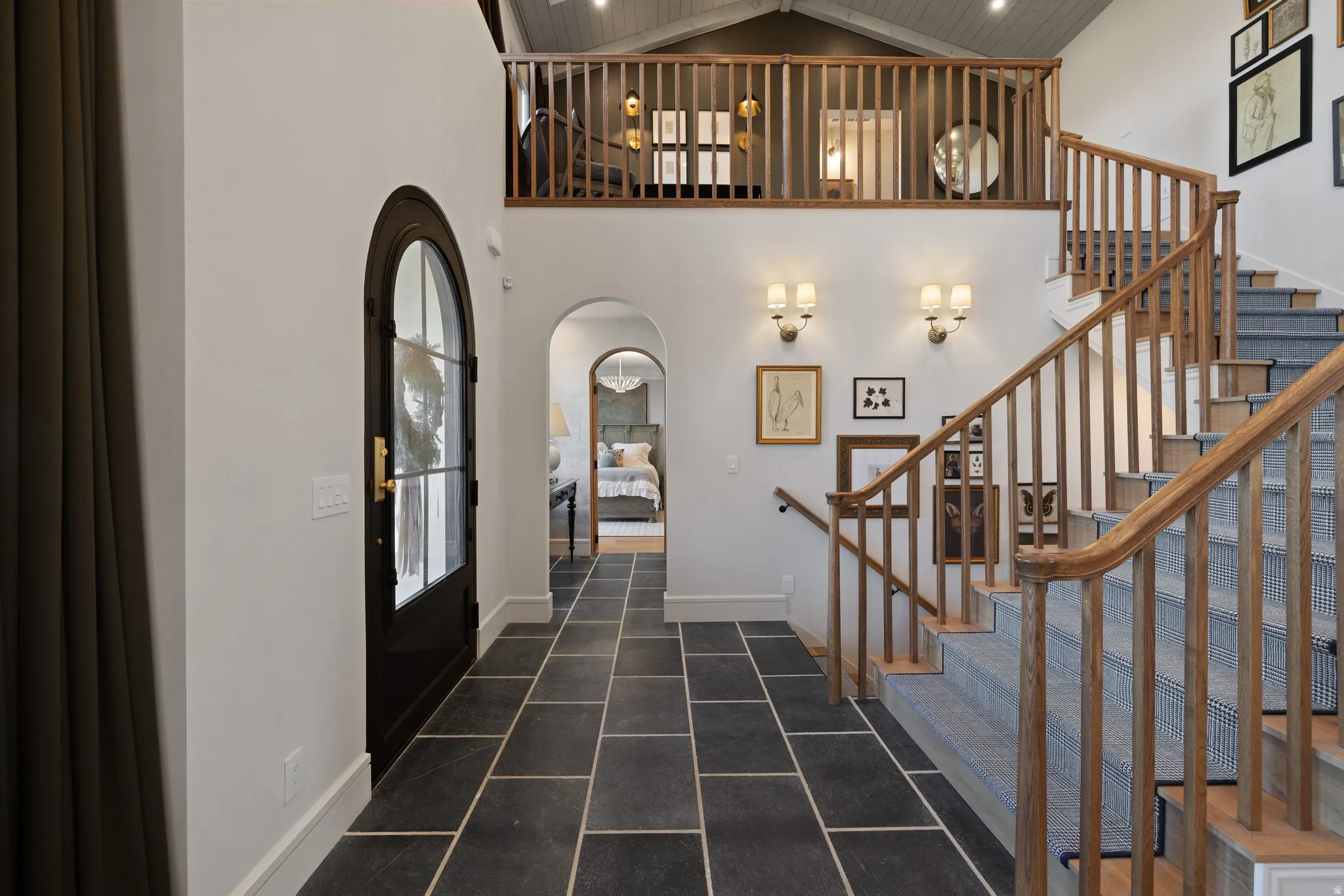 Foyer featuring large format tile flooring, an arched entry door, and a hardwood staircase with carpet runners