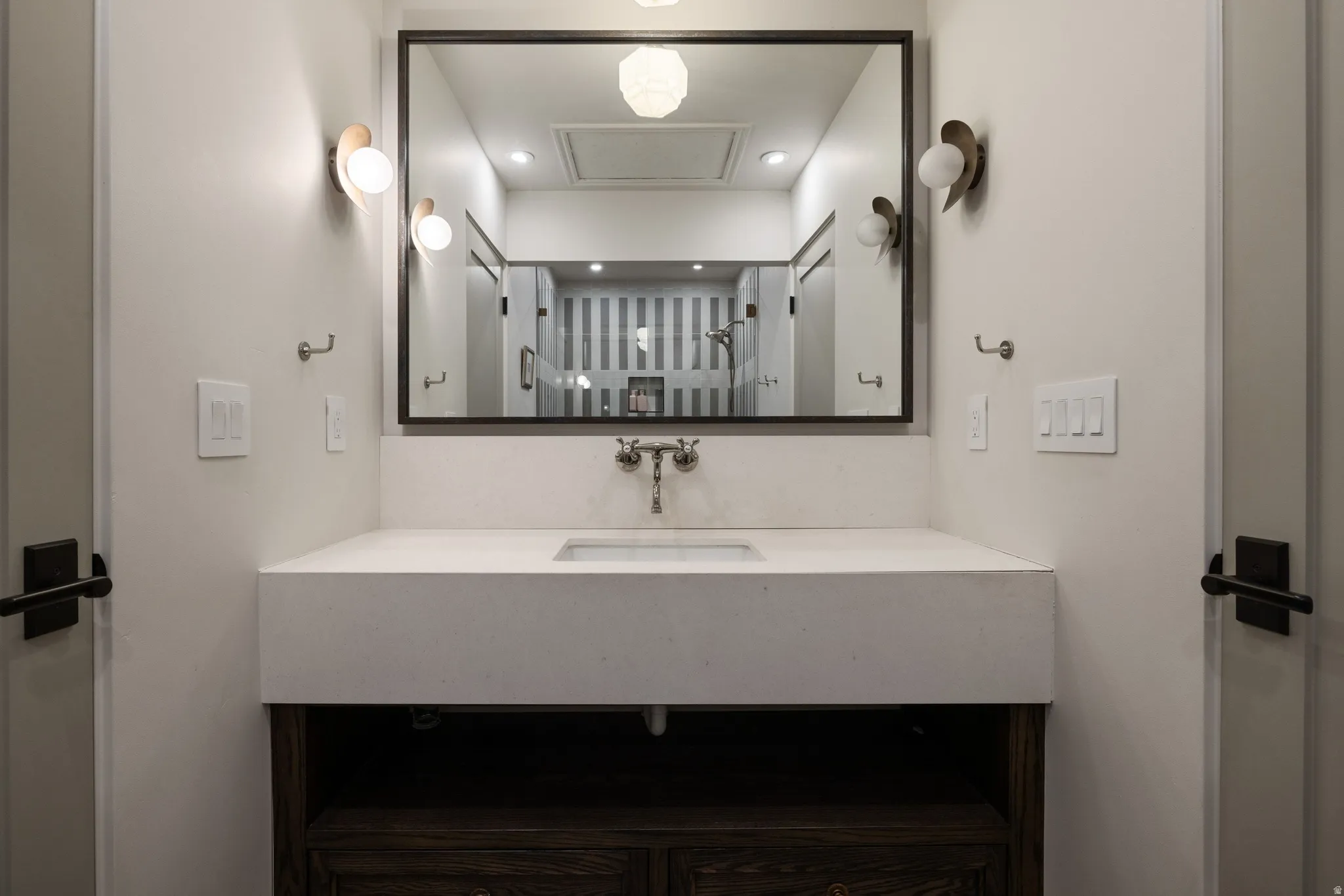 Modern bathroom vanity featuring a clean-lined white countertop with integrated sink, matte black hardware accents, and a framed mirror with integrated lighting