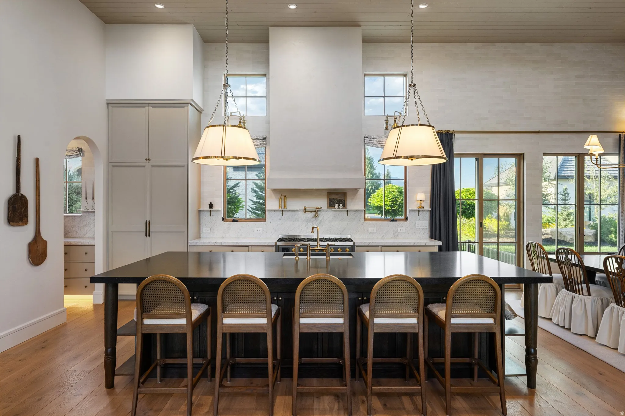 Chef's kitchen featuring a large center island with seating for five, professional-grade gas range, stainless steel appliances, white cabinetry with shaker-style doors, pendant lighting, and expansive countertop workspace