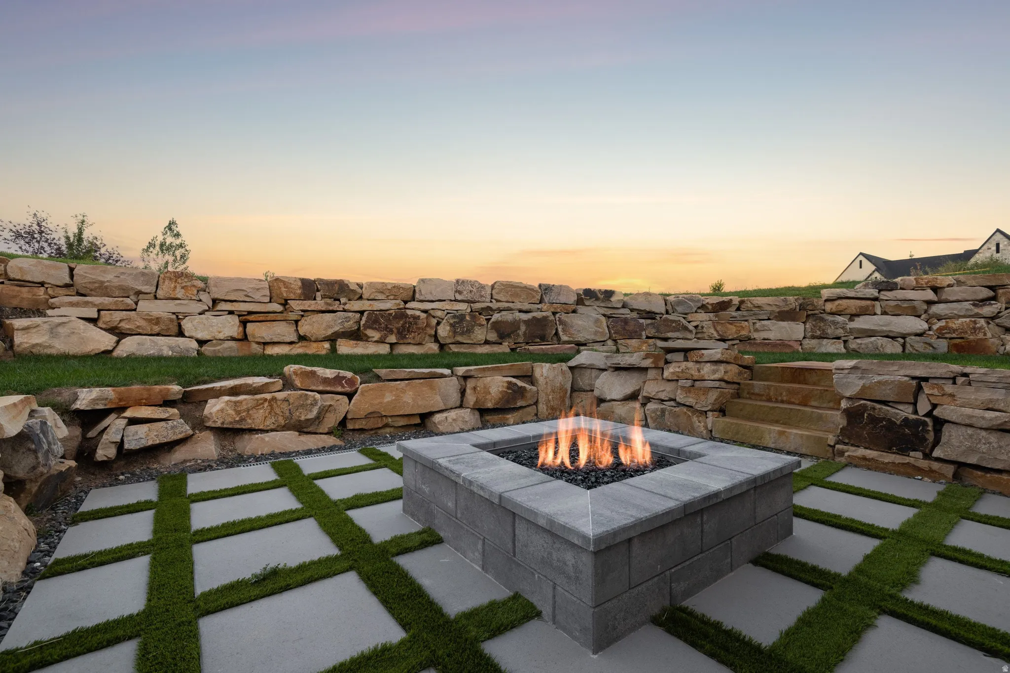 Outdoor living space featuring a built-in fire pit, stone retaining walls, and a paver patio with artificial turf accents