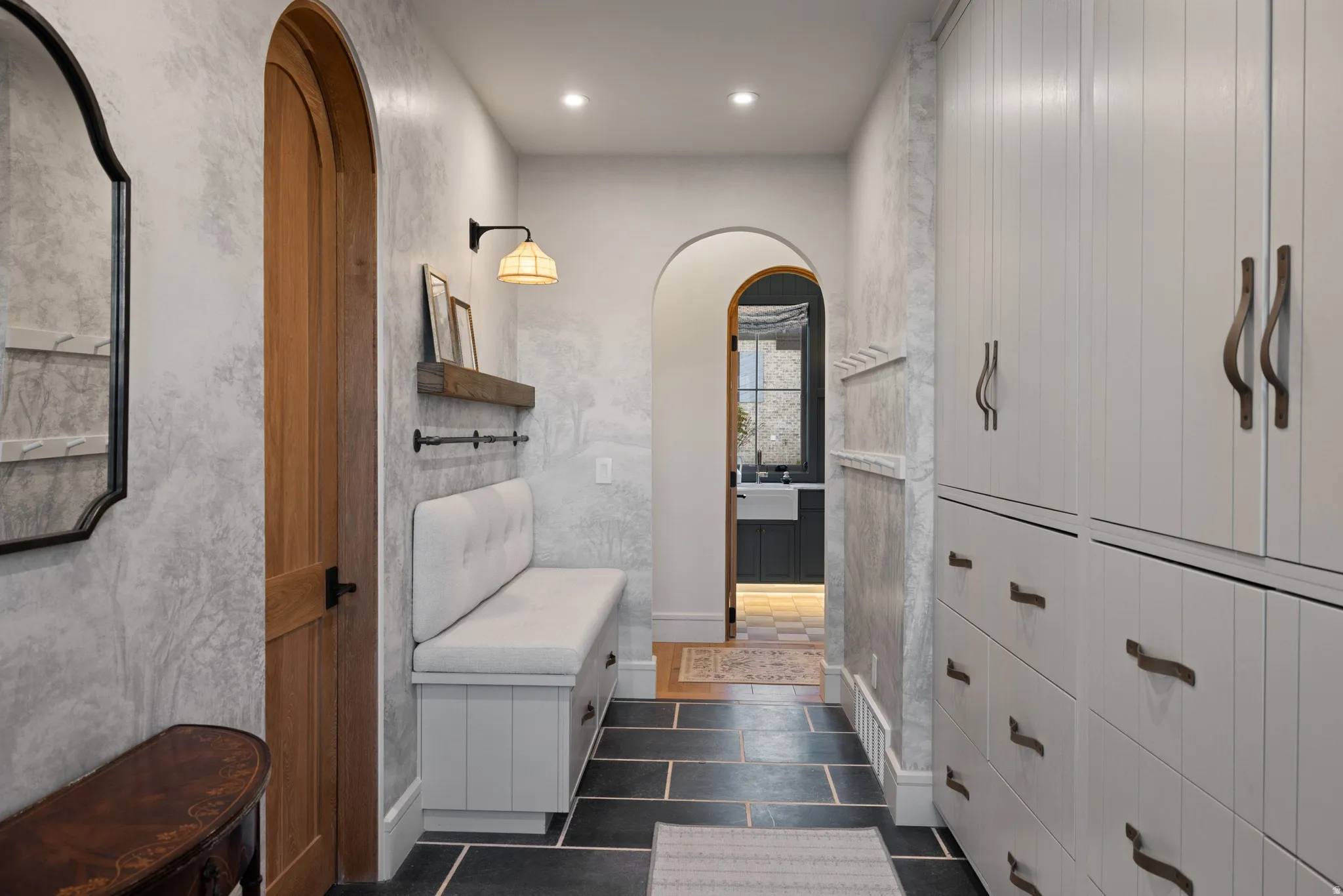 Arched doorway with a wood door, built-in bench seating, recessed lighting, and slate tile flooring