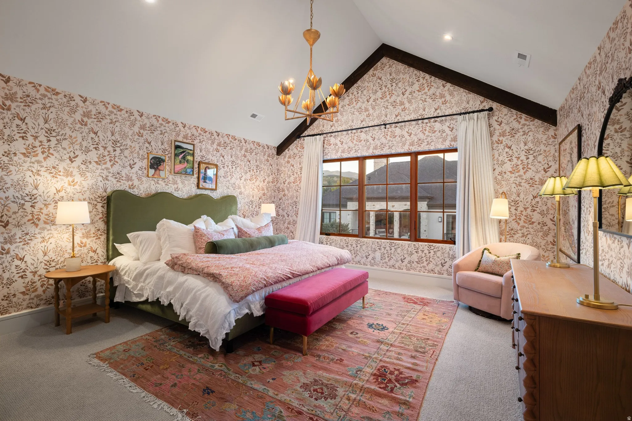 Vaulted ceiling with exposed wood beams, large multi-pane window, patterned wallpaper, wall-mounted chandelier, and recessed lighting