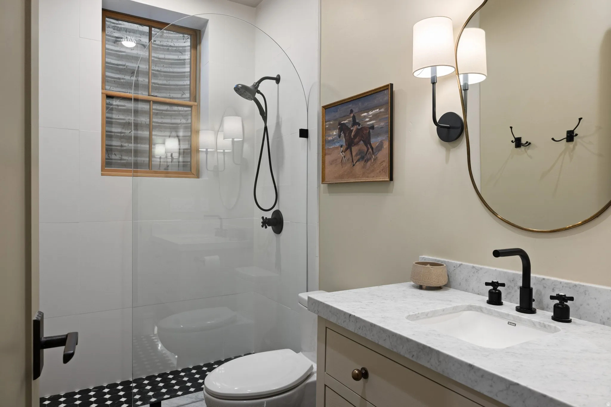 Walk-in shower with clear glass enclosure and black and white patterned tile flooring