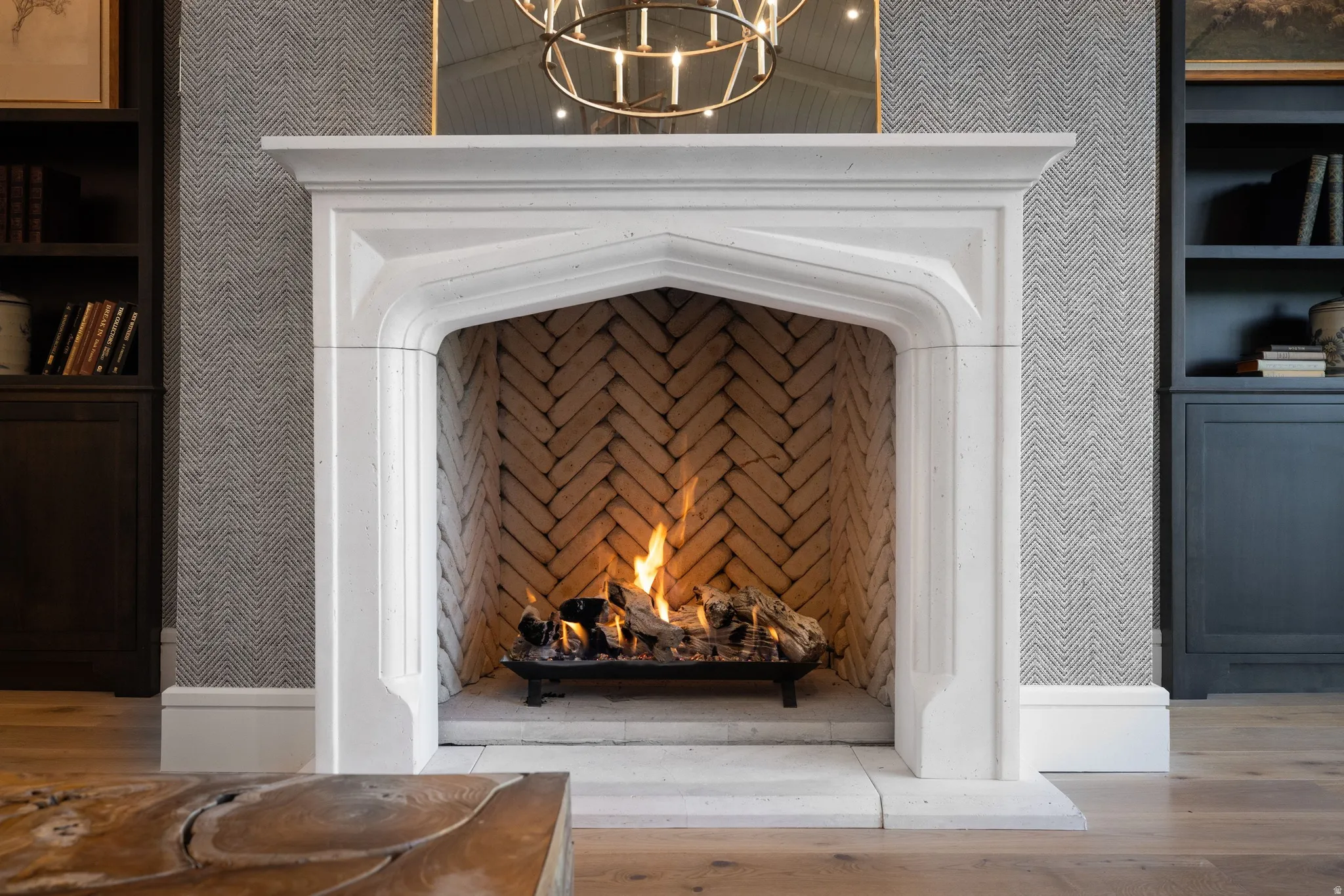 Ornate fireplace with a herringbone brick interior, carved stone surround, and light wood-finish flooring