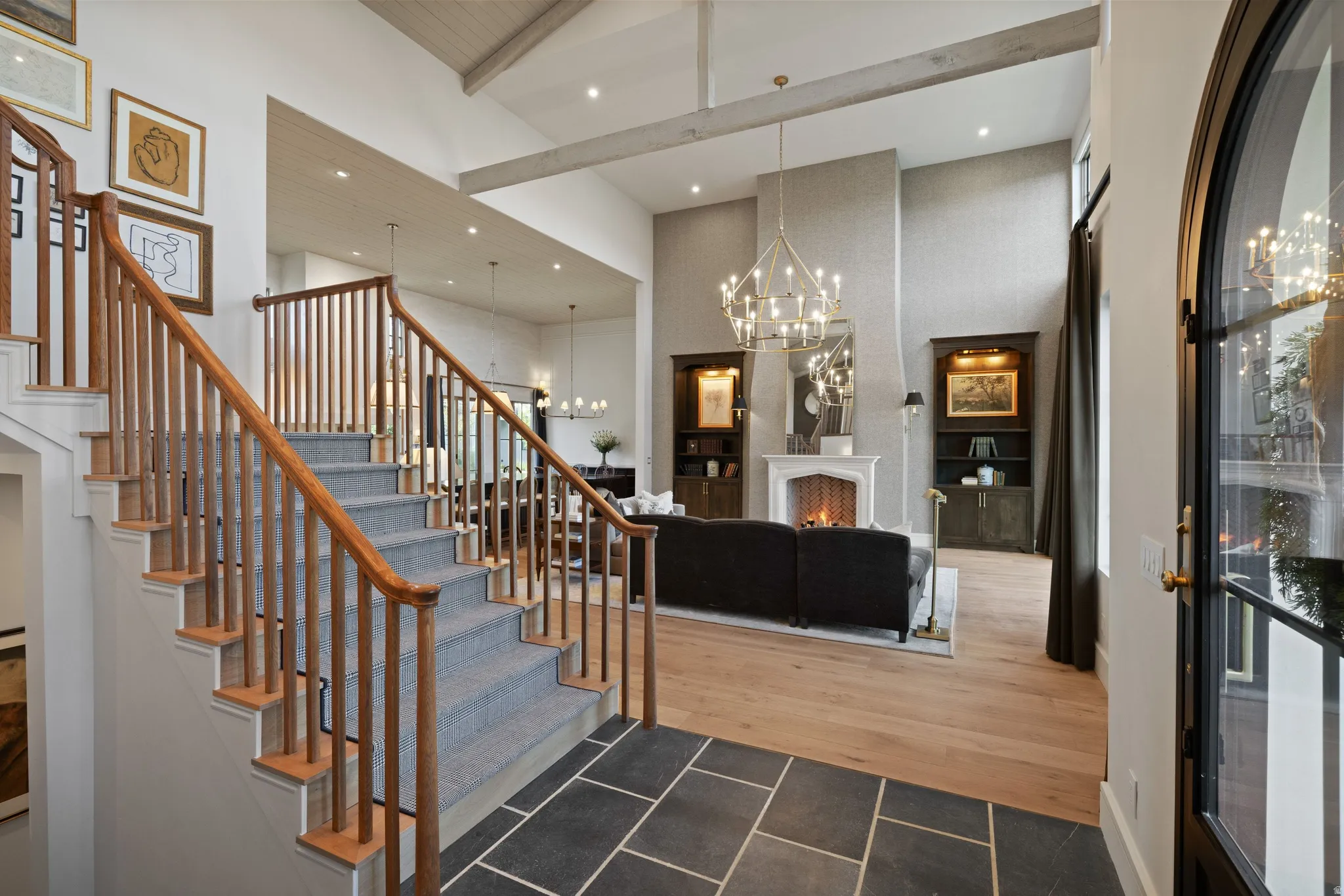 Entry foyer with bluestone tile flooring, wood staircase with carpet treads, and a black arch-top door