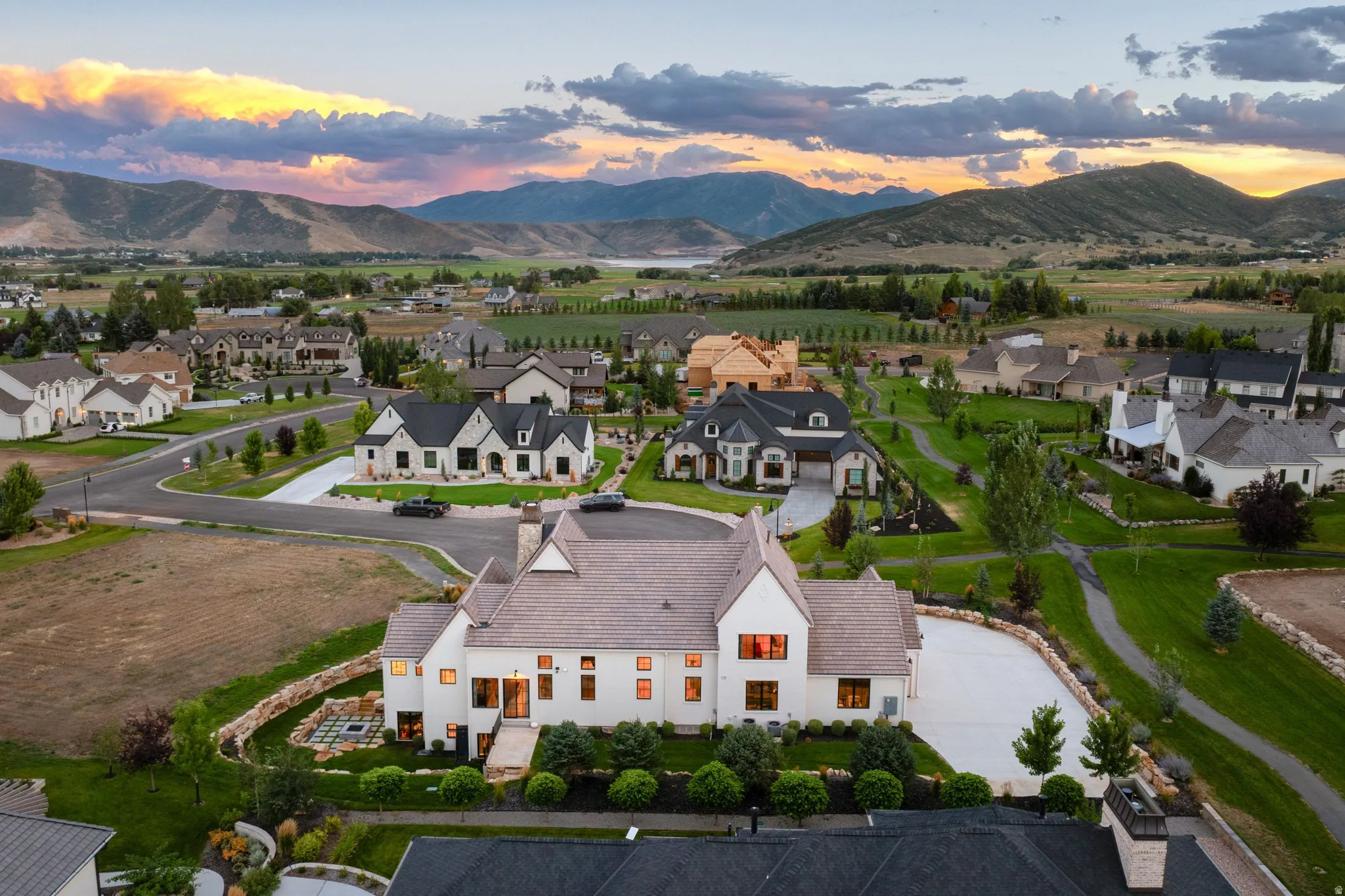 White exterior residence with multiple gables and a light-toned roof, featuring a paved driveway and landscaped grounds, set against a backdrop of distant mountains and a body of water