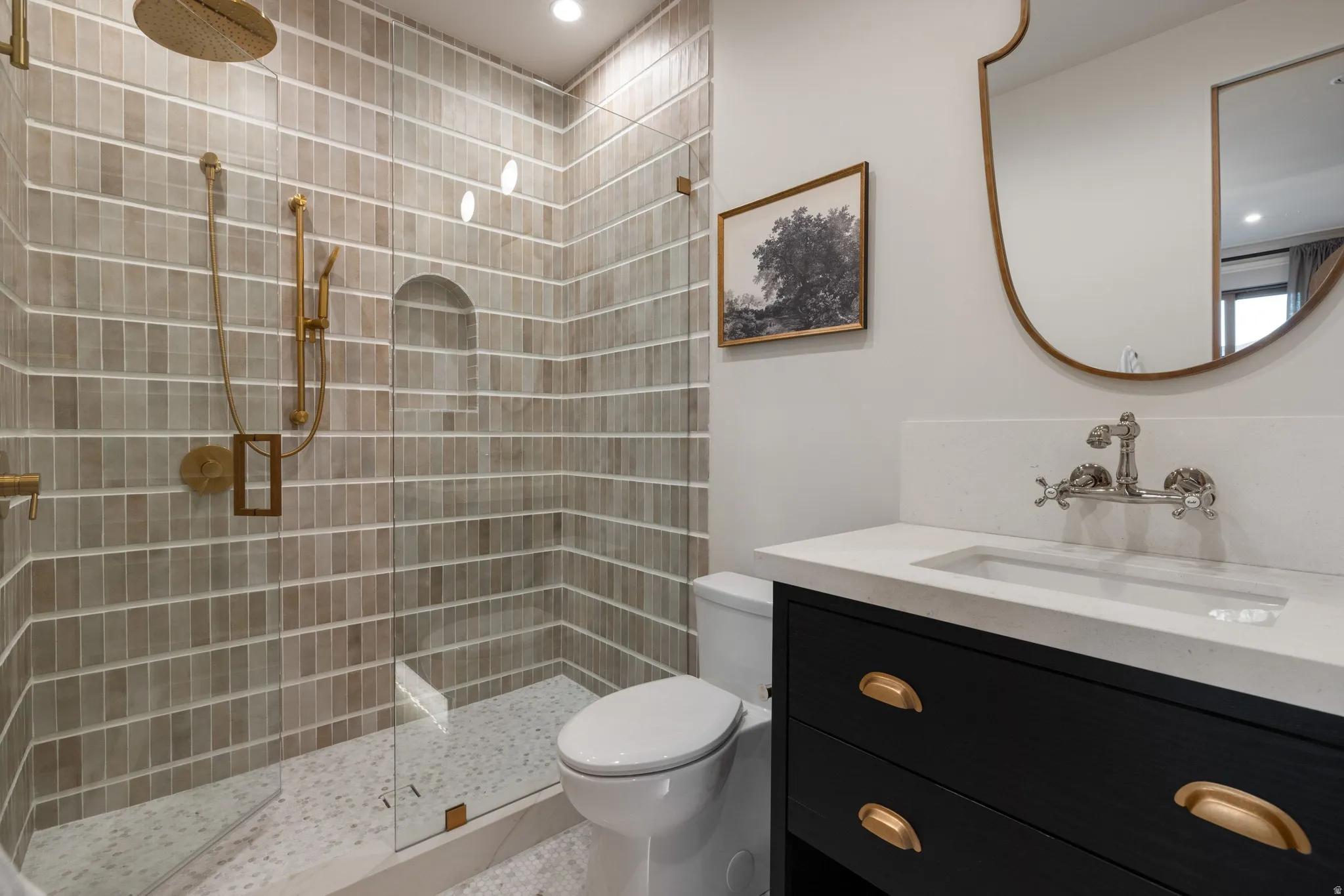 Spa-inspired bathroom featuring subway tile shower enclosure with brass fixtures, white quartz countertop, black vanity cabinetry with brass hardware, vessel sink, and brass-framed mirror