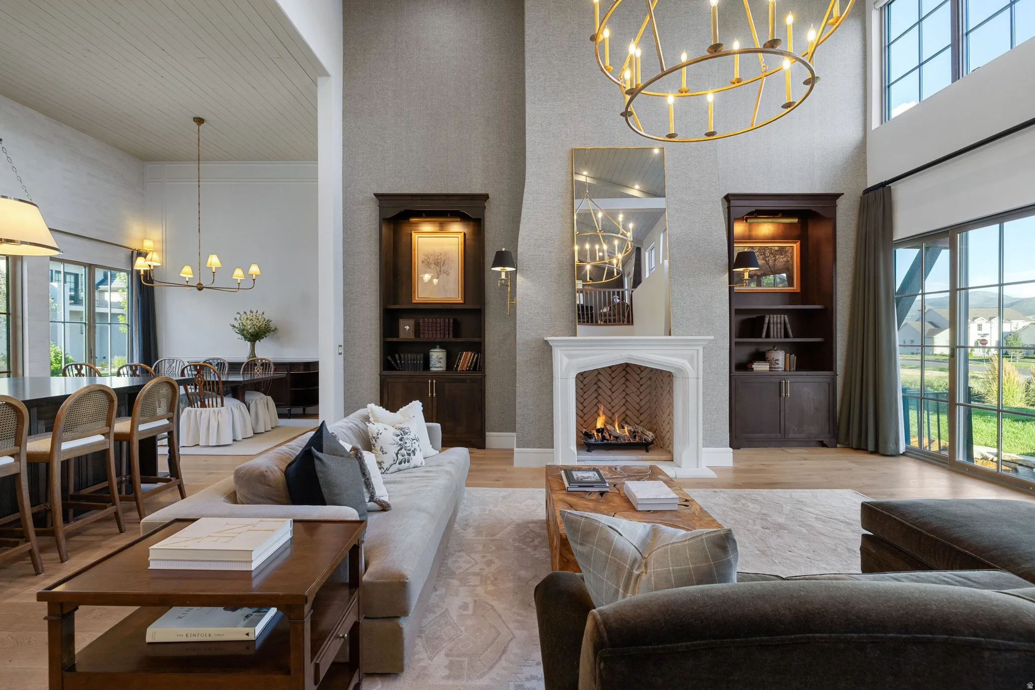 Soaring two-story great room with coffered ceiling, gas fireplace with white surround and dark wood-finish mantelpiece, and abundant natural light from oversized windows and glass doors