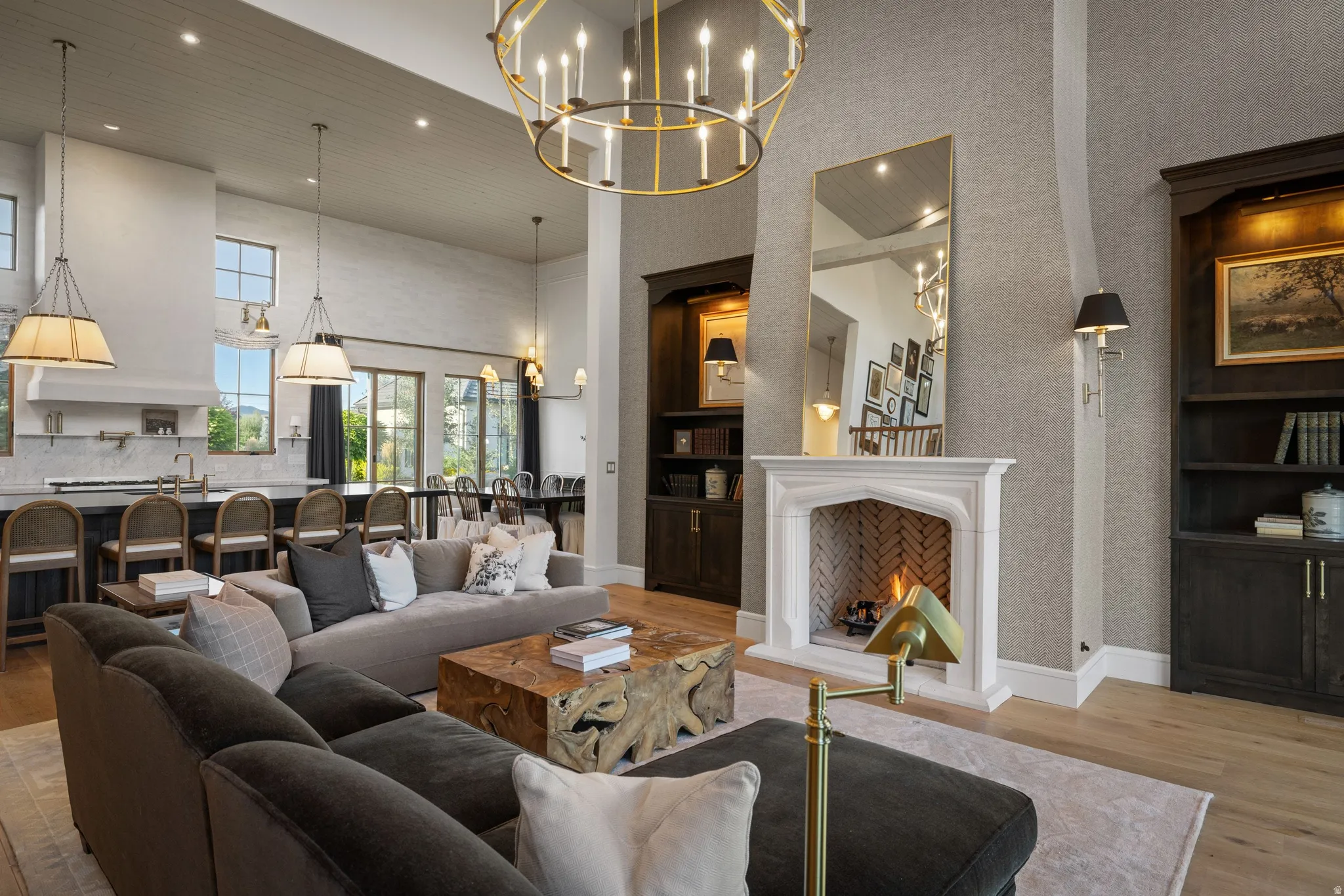 Open-concept living space featuring soaring ceilings, a gas fireplace with white surround and herringbone detailing, and a geometric brass chandelier