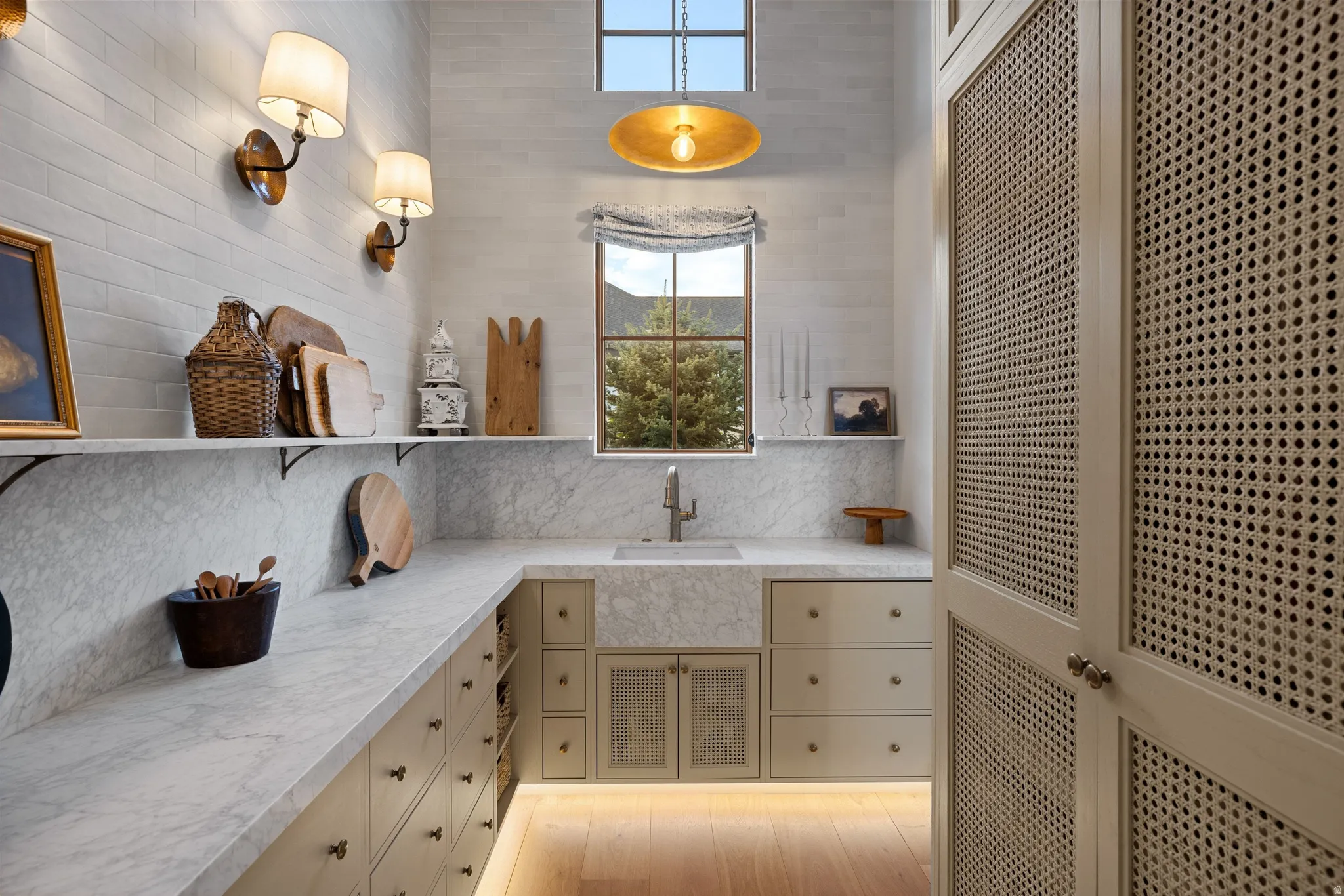 Built-in cabinetry with woven door panels and drawers, light wood-finish flooring, undermount lighting, integrated farmhouse sink, and a high window