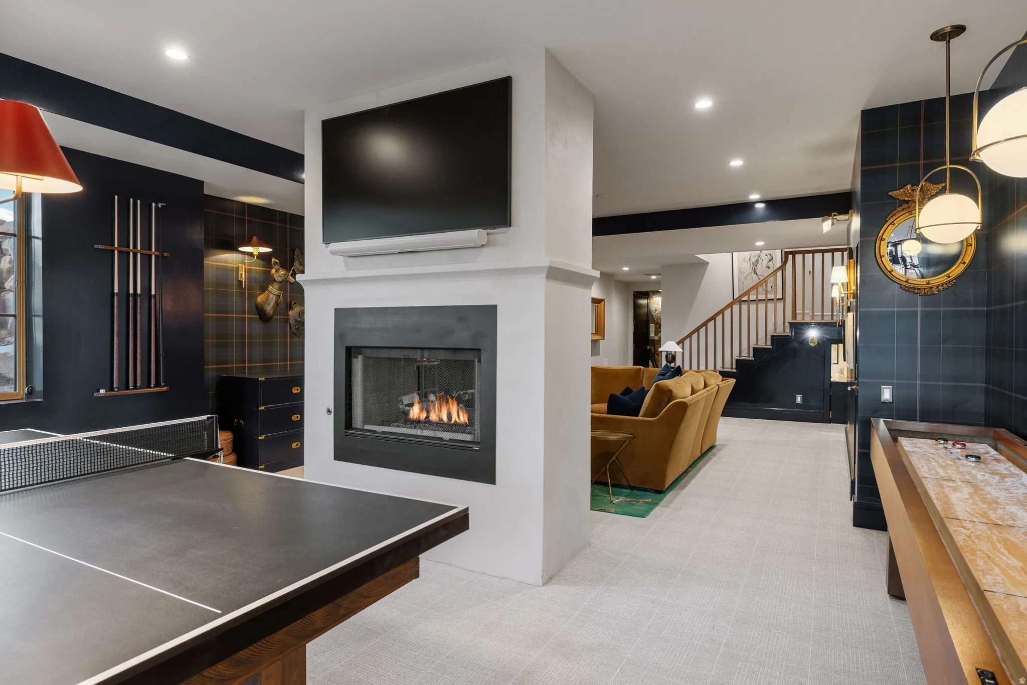 Sophisticated recreation space anchored by a gas fireplace with built-in television, complemented by a slate-topped pool table, light-filled ceiling with recessed and pendant lighting, and navy accent walls with white trim detailing throughout the open-co