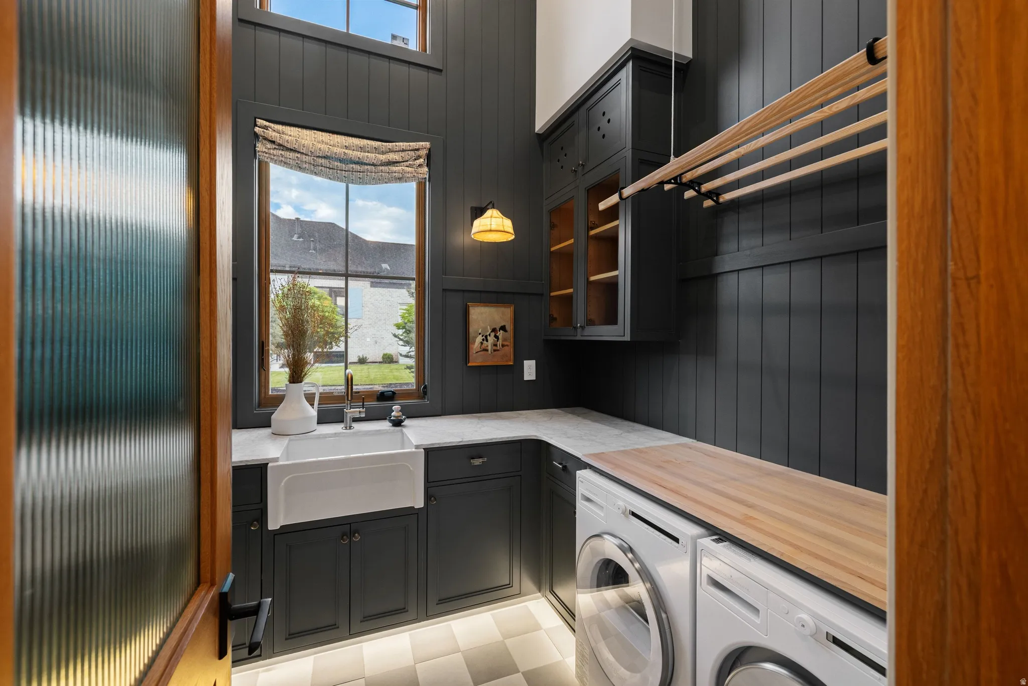 Vertical shiplap wall treatment, built-in cabinetry, farmhouse sink, wood-finish countertop, and checkered floor tiles