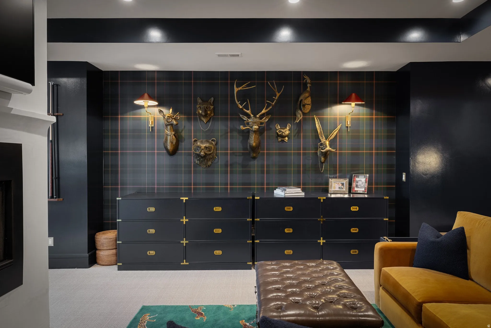 Sophisticated entertainment space featuring custom black cabinetry with brass hardware, grid-pattern wall paneling with integrated display shelving, recessed ceiling lighting, and a tufted upholstered ottoman with complementary seating