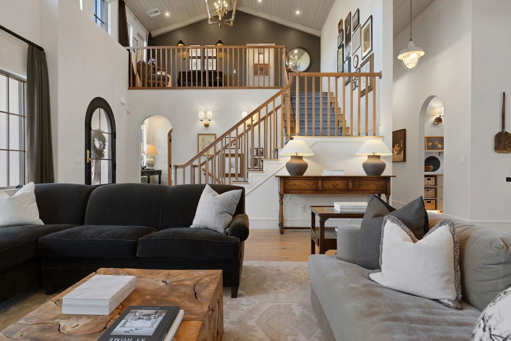 Soaring two-story great room with vaulted ceilings, abundant natural light from multiple windows, and a floating mezzanine level with wood railings