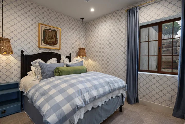 Charming bedroom featuring a black metal bed frame, patterned wallcovering throughout, pendant lighting fixtures, and wood-frame French doors with multi-pane glazing