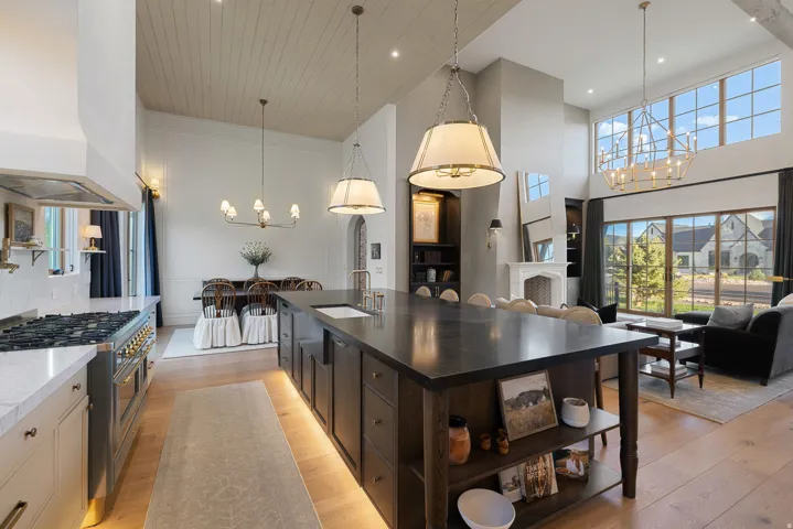 Open-concept kitchen and living area featuring a large center island with dark wood cabinetry and open shelving, pendant lighting, stainless steel appliances including a professional-style range, white cabinetry, wood-finish flooring, and expansive window