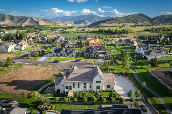 Elegant residential estate set on expansive grounds featuring a distinctive peaked-roof architectural design with light-colored exterior, mature landscaping with manicured lawn and established trees, curved driveway with paved entry, and mountain vistas a