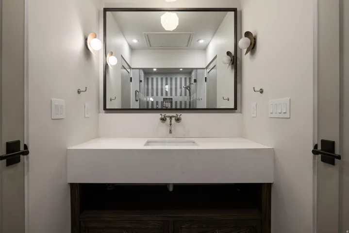 Modern bathroom vanity featuring a clean-lined white countertop with integrated sink, matte black hardware accents, and a framed mirror with integrated lighting