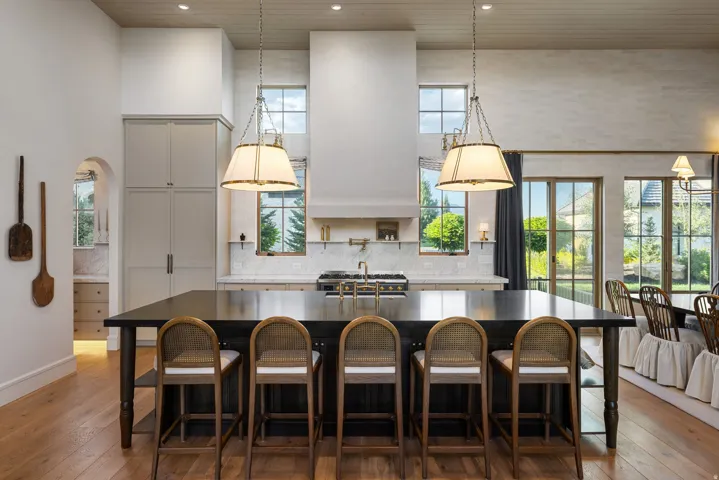 Chef's kitchen featuring a large center island with seating for five, professional-grade gas range, stainless steel appliances, white cabinetry with shaker-style doors, pendant lighting, and expansive countertop workspace