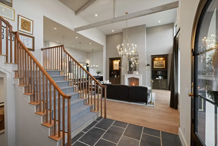 Entry foyer with bluestone tile flooring, wood staircase with carpet treads, and a black arch-top door