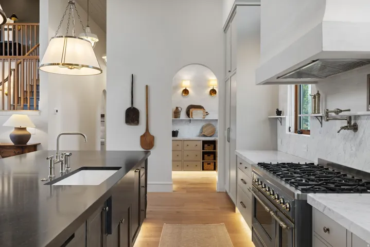 Chef's kitchen featuring professional-grade dual fuel range with six burners, stainless steel countertops, marble subway tile backsplash, custom cabinetry with integrated storage, and pendant lighting suspended from coffered ceiling details