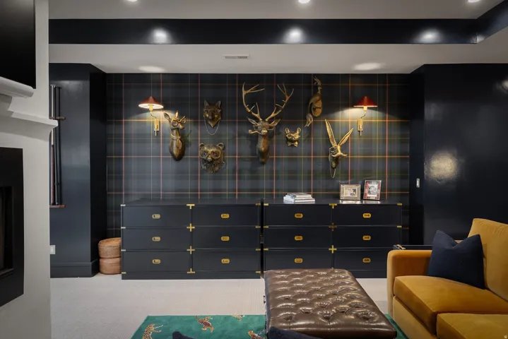 Sophisticated entertainment space featuring custom black cabinetry with brass hardware, grid-pattern wall paneling with integrated display shelving, recessed ceiling lighting, and a tufted upholstered ottoman with complementary seating
