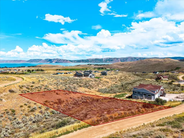 Expansive rural property featuring a substantial cleared and graded lot with defined boundaries, a modern residence with dark exterior cladding and pitched roofline, and panoramic vistas encompassing distant mountains, coastline, and rolling terrain