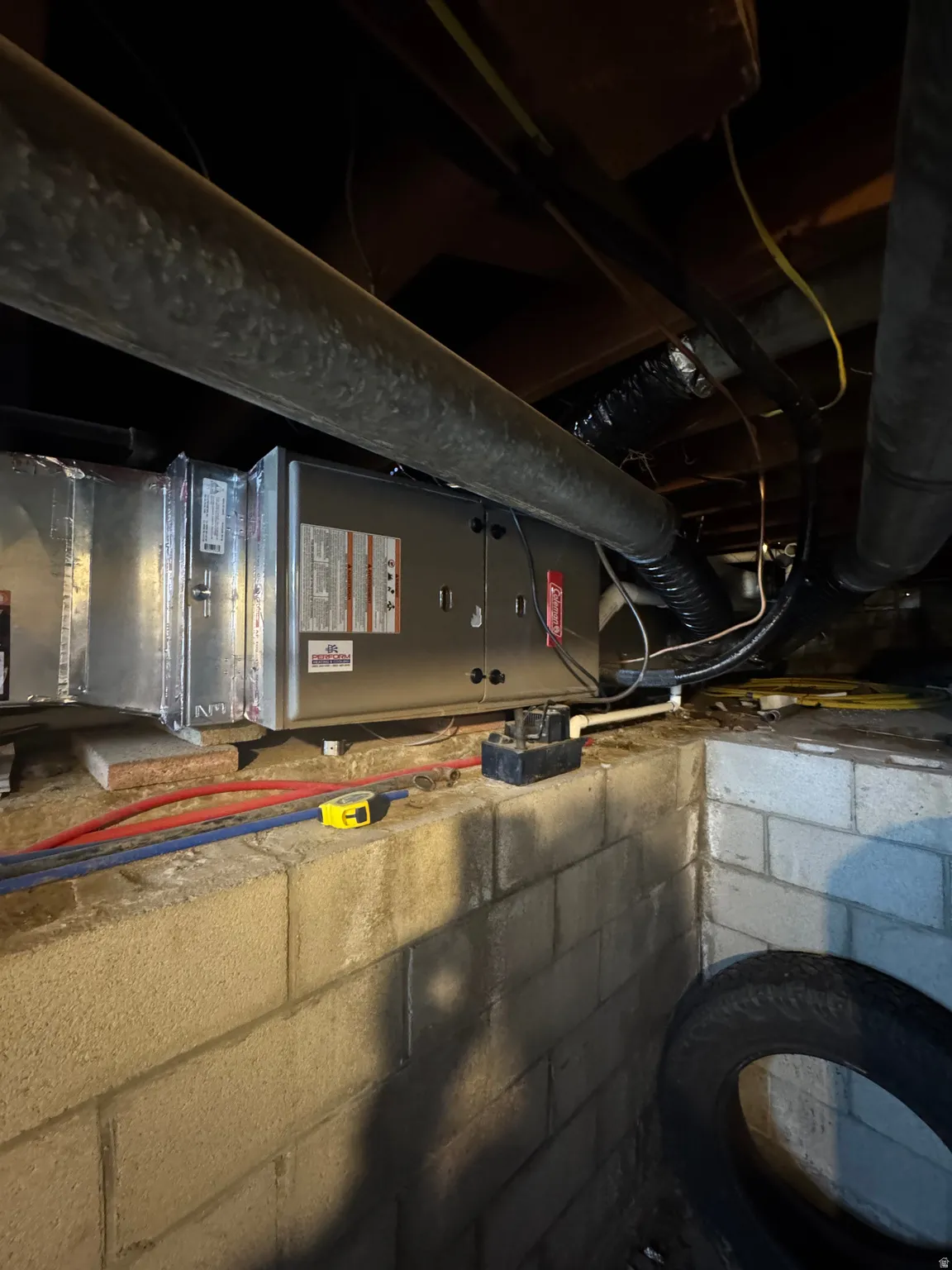 HVAC unit with exposed ductwork, supported by concrete block foundation walls