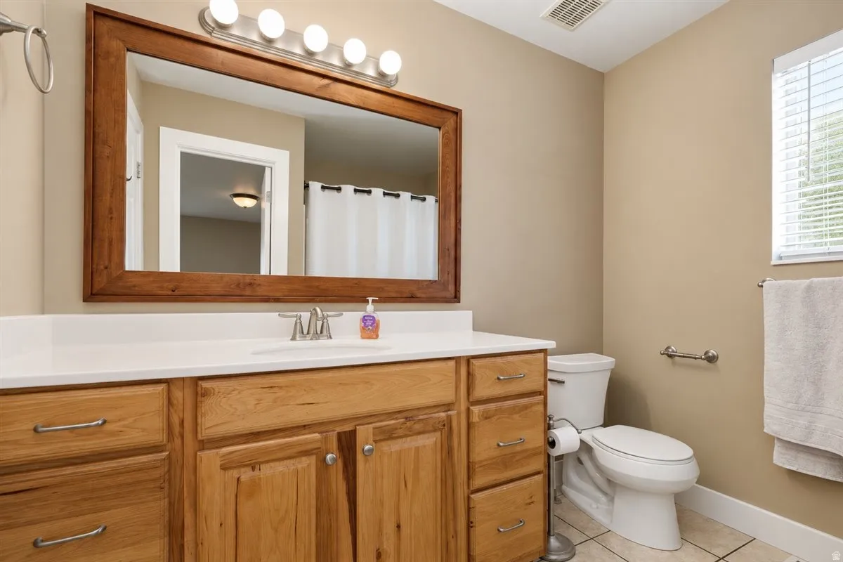 Wood-finish vanity with a white countertop, framed mirror, and tile flooring