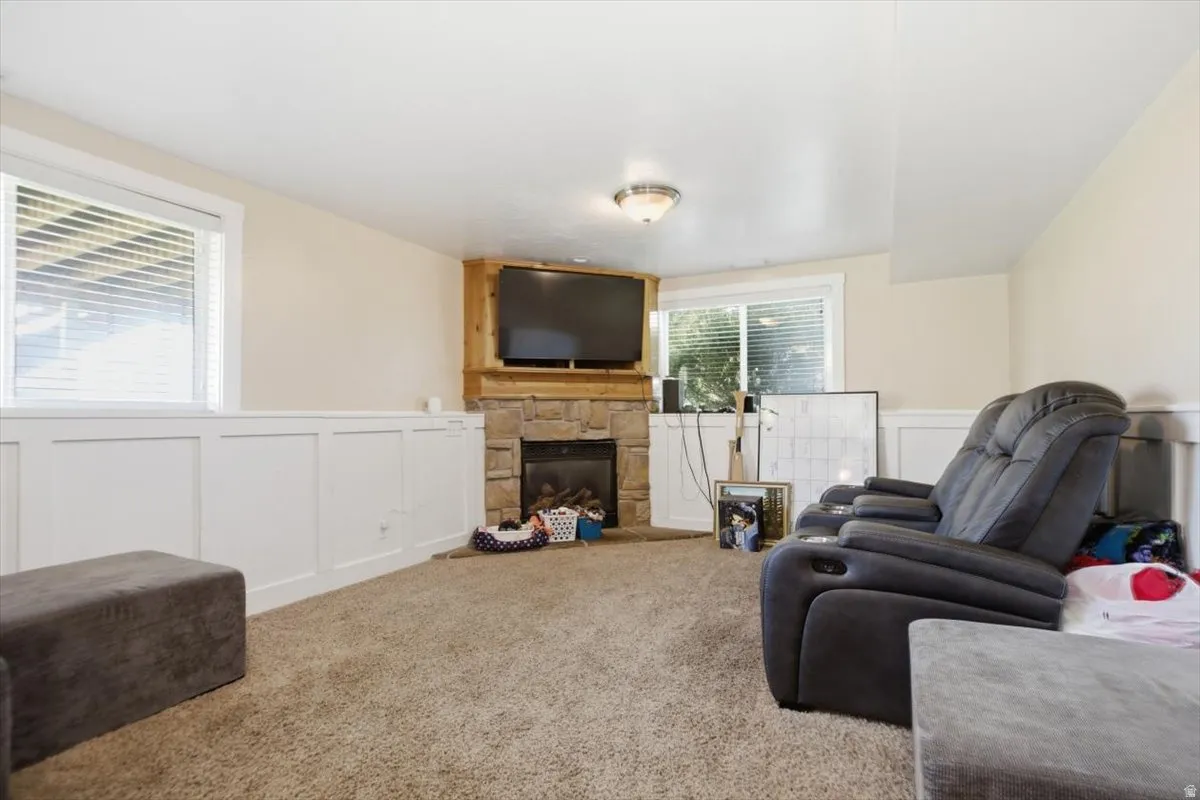 Stone fireplace with a wood mantel, soft carpet flooring, and white paneled wainscoting