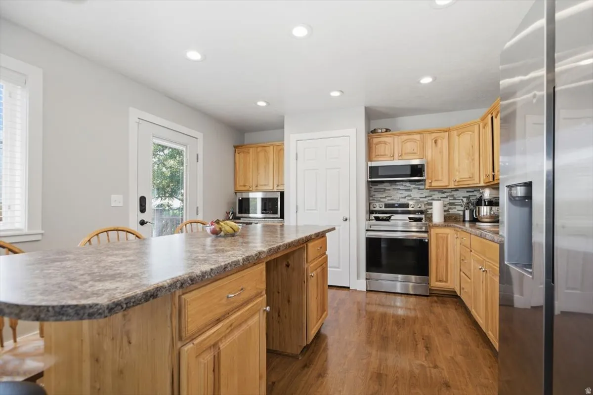 Wood-finish flooring, recessed lighting, wood cabinetry, stainless steel appliances, and a tiled backsplash