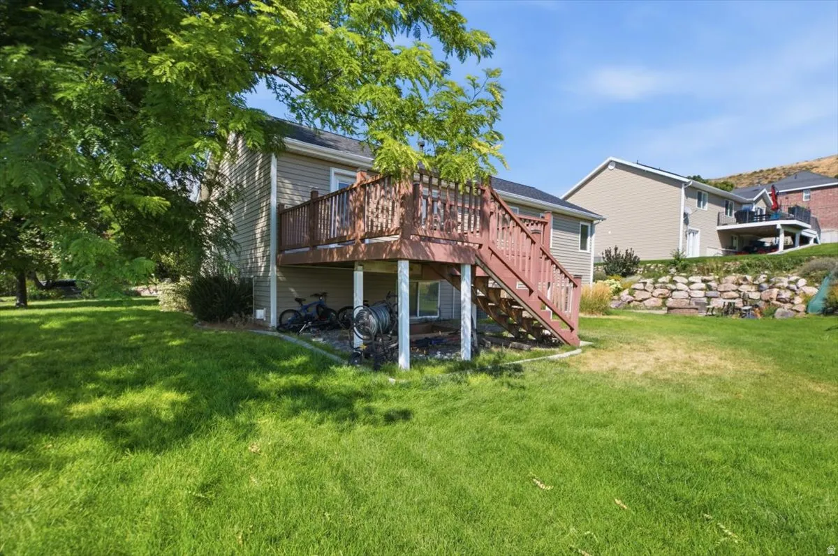 Spacious backyard oasis featuring a mature shade tree, lush manicured lawn, and a multi-level wood deck with stairs providing outdoor entertaining space
