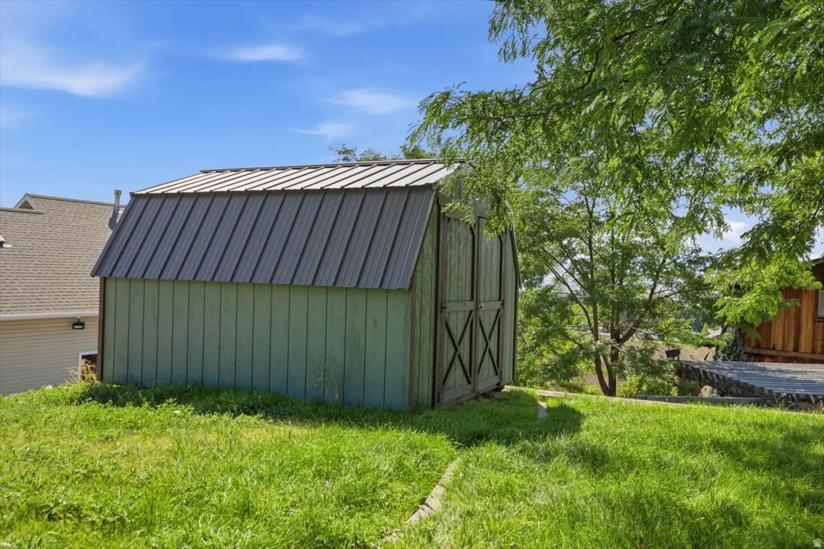 Green-sided utility shed with a metal roof and double doors, situated on a sloped grassy area