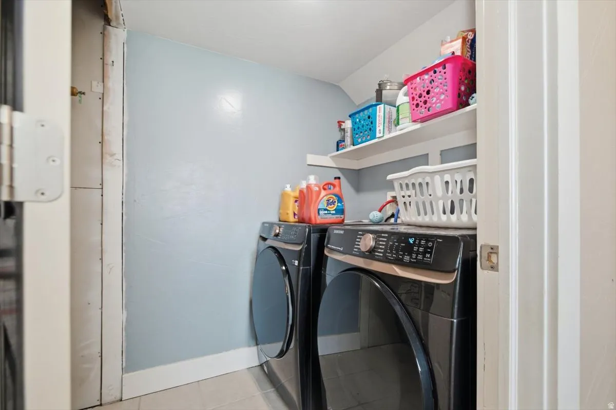 Dedicated laundry room featuring side-by-side black front-load washer and dryer with digital controls, light blue accent wall, white shelving with storage baskets, and overhead recessed lighting for optimal functionality