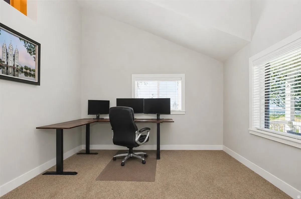 Vaulted ceiling, two windows with blinds, light gray wall paint, and carpeting