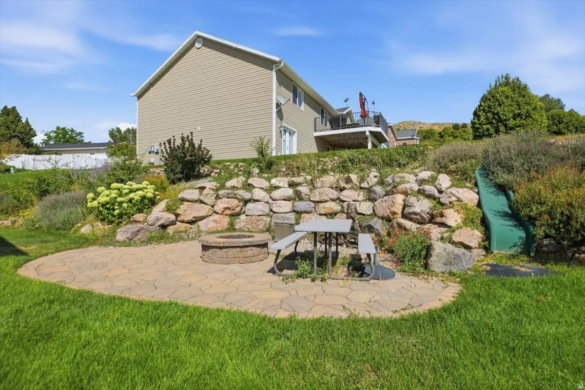 Expansive backyard retreat featuring a circular stone-paved patio, tiered natural stone retaining walls with integrated planting beds, mature landscaping, and manicured lawn