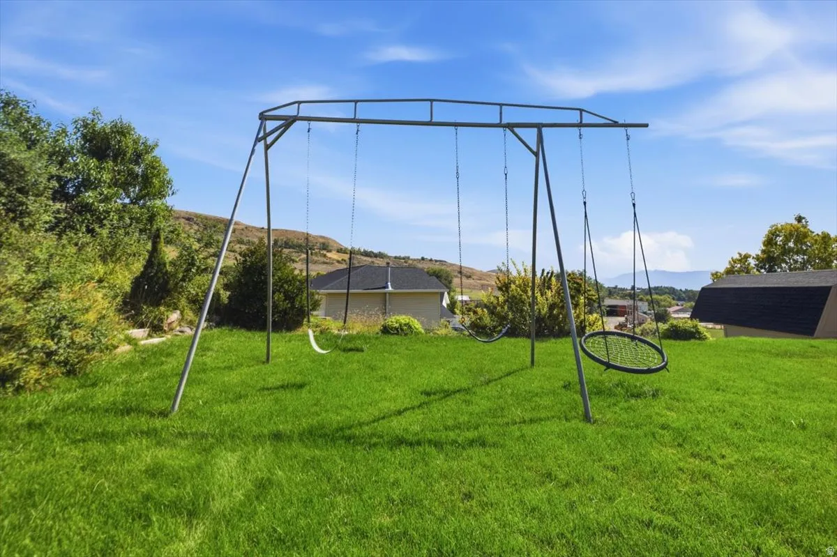 Expansive lawn with mature landscaping and established trees, complemented by a metal swing set structure with multiple swings