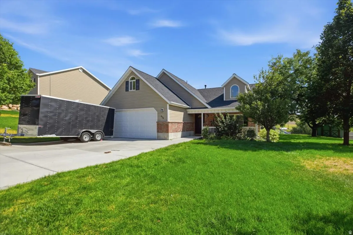 Charming brick and siding home featuring a spacious two-car garage, manicured lawn with mature shade trees, and a welcoming front elevation with gabled roofline and decorative dormer detailing