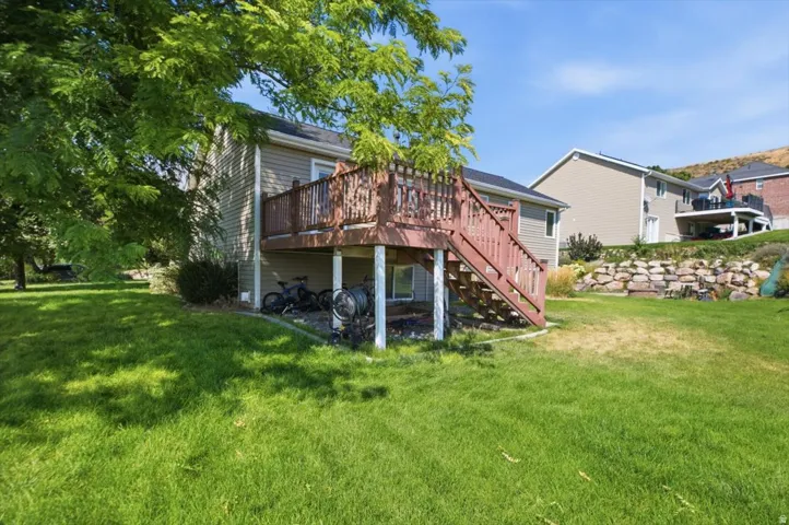 Spacious backyard oasis featuring a mature shade tree, lush manicured lawn, and a multi-level wood deck with stairs providing outdoor entertaining space