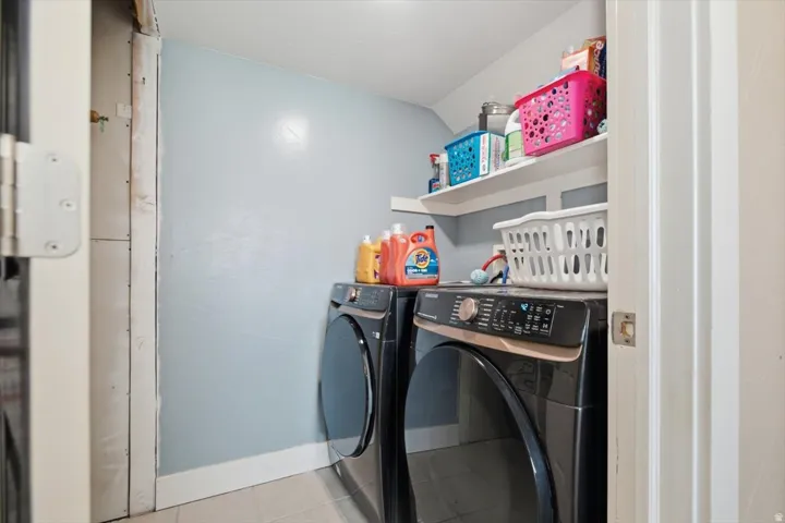 Dedicated laundry room featuring side-by-side black front-load washer and dryer with digital controls, light blue accent wall, white shelving with storage baskets, and overhead recessed lighting for optimal functionality