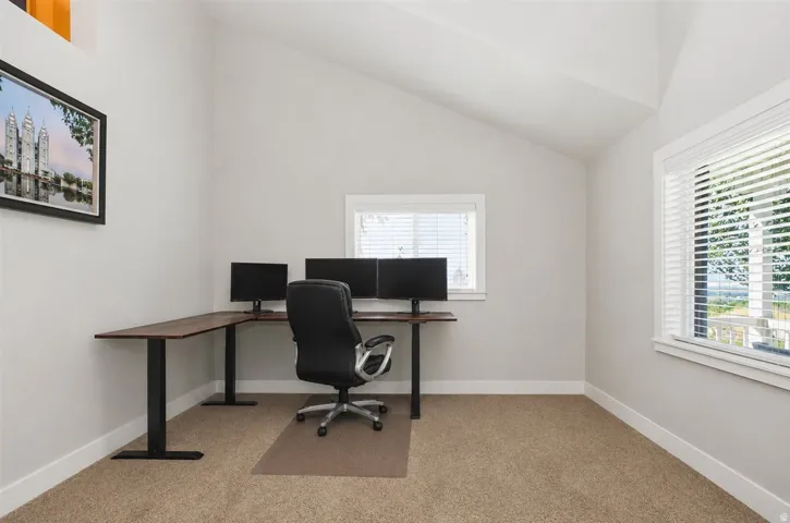 Vaulted ceiling, two windows with blinds, light gray wall paint, and carpeting