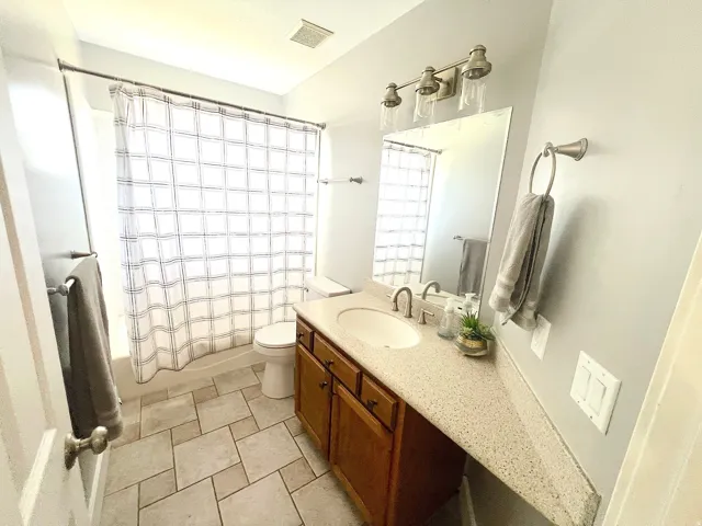 Bathroom featuring a vanity with a single sink, light-colored countertop, wood-finish cabinetry, and patterned tile flooring