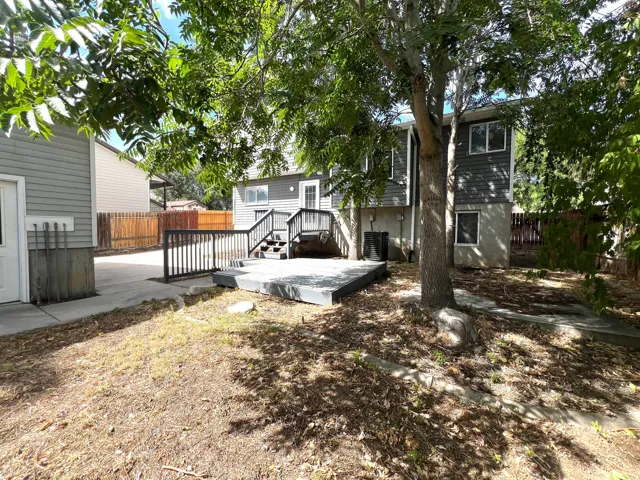 Spacious backyard oasis featuring mature shade trees, a multi-level composite deck with metal railings, and a fire pit area
