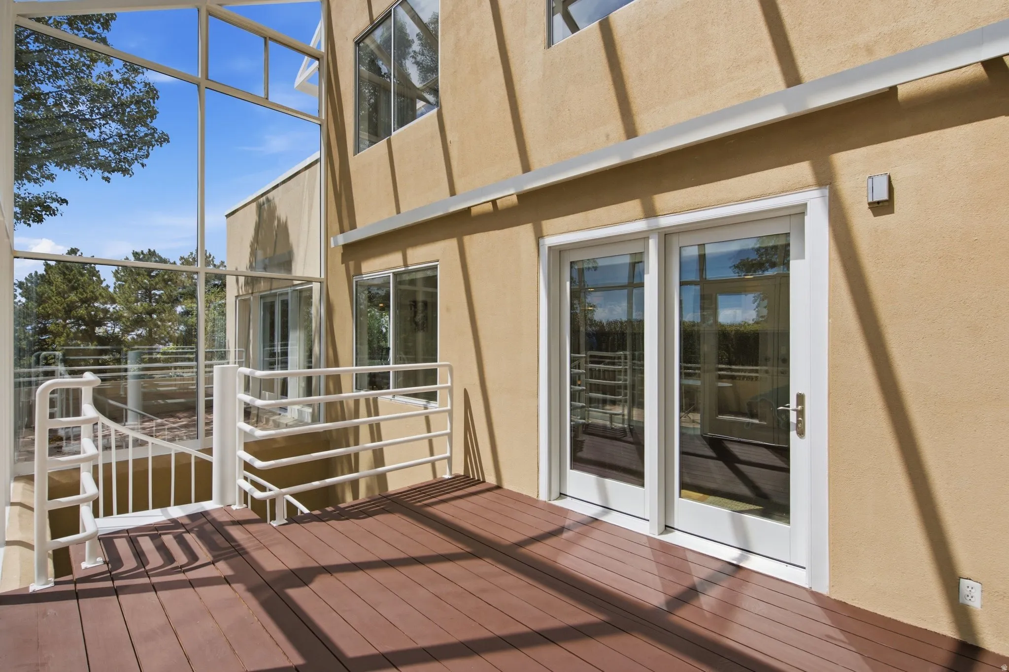 Expansive wood-finish deck with white railings, featuring full-light double doors and a glass enclosure