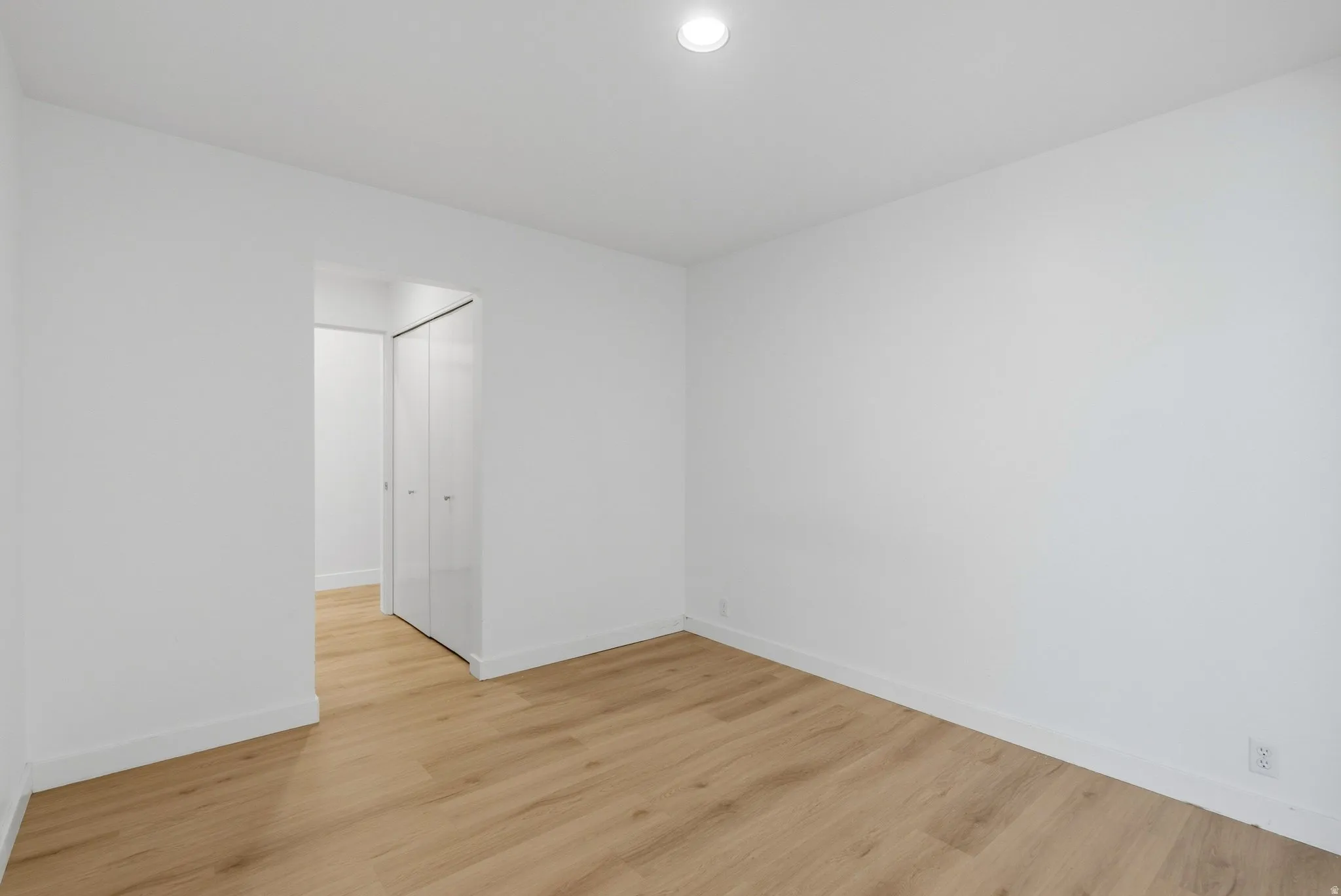 Recessed ceiling lighting, light wood-finish flooring, white walls, and a closet with bifold doors